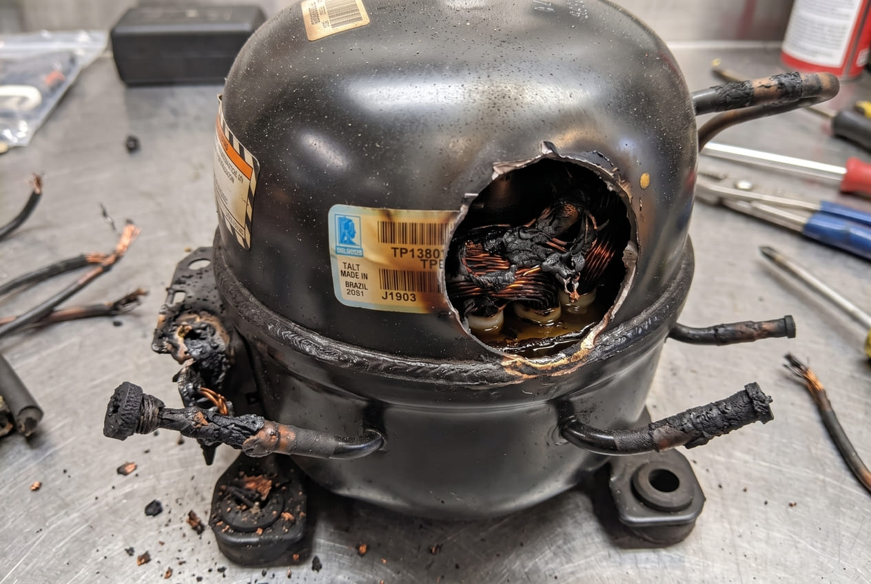 Burned out Amana refrigerator compressor motor showing scorched terminals and internal damage